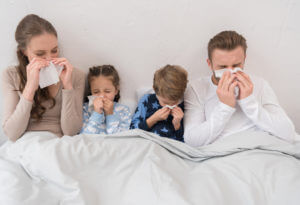 Sick parents and children lying in a bed and blowing noses in napkins